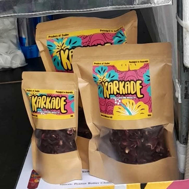 Three kraft pouches of Karkade dried hibiscus with window panels showing the deep red dried calyces inside, labelled Product of Sudan, packaged in Australia