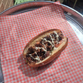 Smoked brisket shawarma in a fresh roll with garlic tahini, tomato and onion, on red checked paper