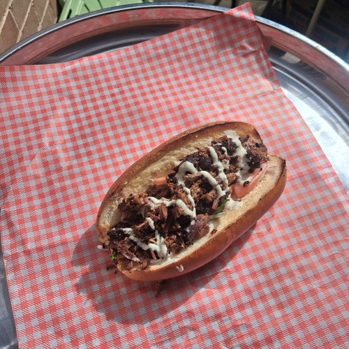 Smoked brisket shawarma in a fresh roll with garlic tahini, tomato and onion, on red checked paper